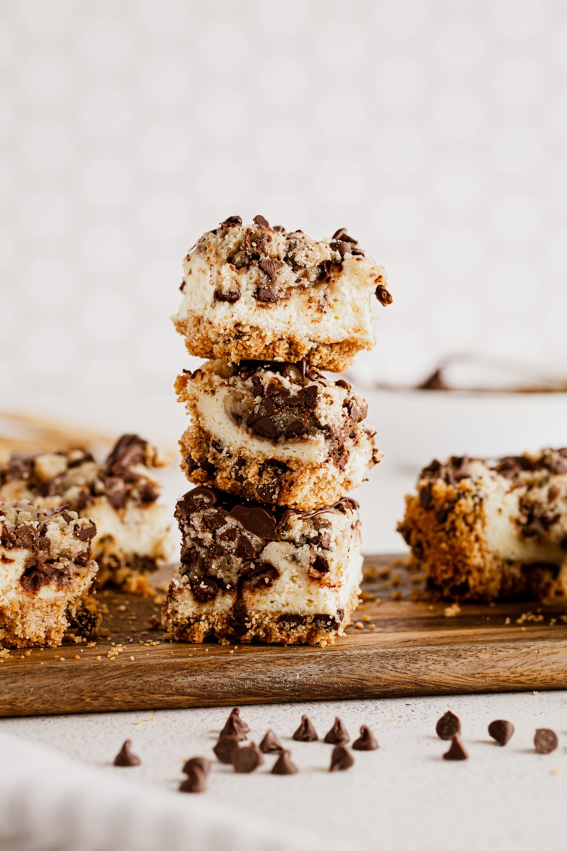 Three cookie dough cheesecake bars stacked on wood board