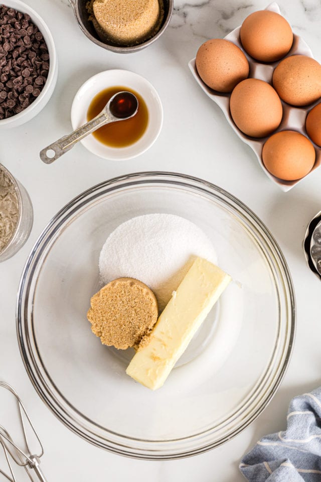 Overhead view of butter, brown sugar, and white sugar in glass mixing bowl