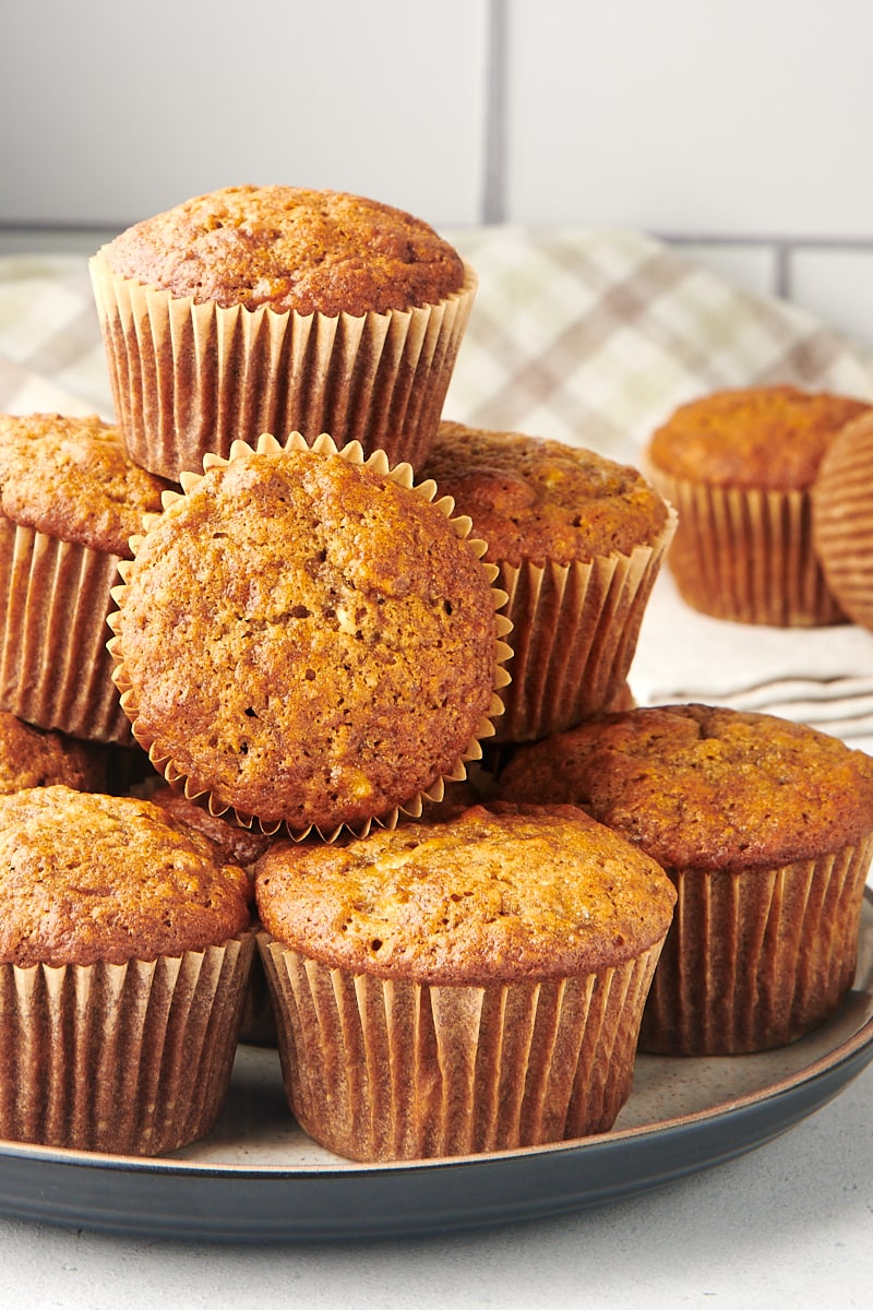 Pile of banana nut muffins in wrappers on a white and brown speckled plate.