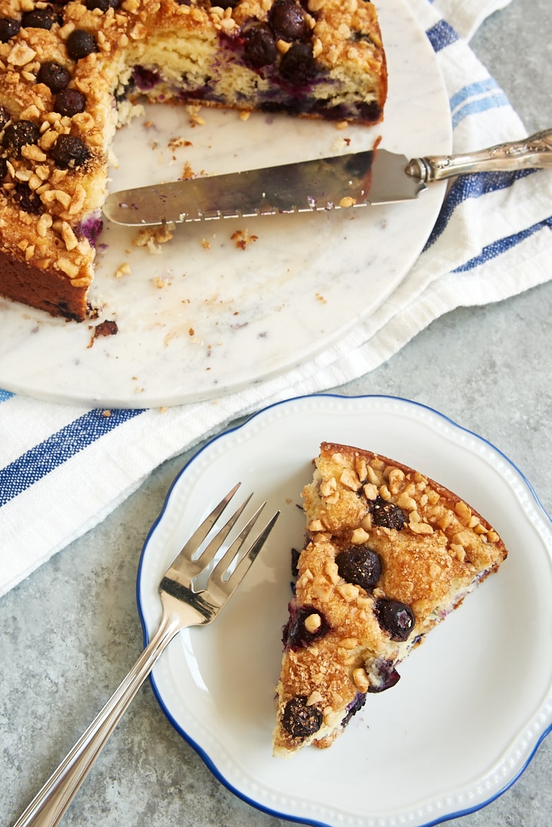 overhead view of a slice of Blueberry Coffee Cake on a blue-rimmed white plate with the remaining cake alongside