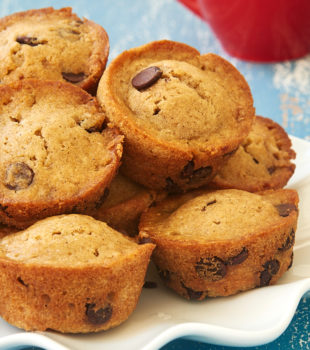 pile of Chocolate Chip Muffins on a white plate with a red mug in the background