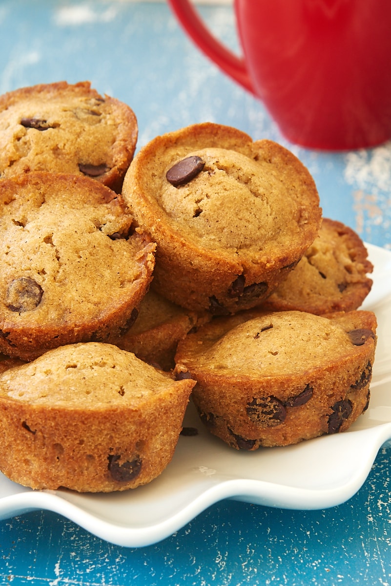 pile of Chocolate Chip Muffins on a white plate with a red mug in the background