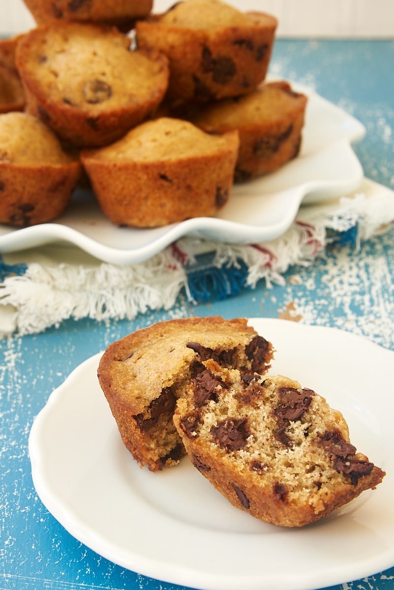 two halves of a Chocolate Chip Muffin on a white plate with more muffins on a plate in the background