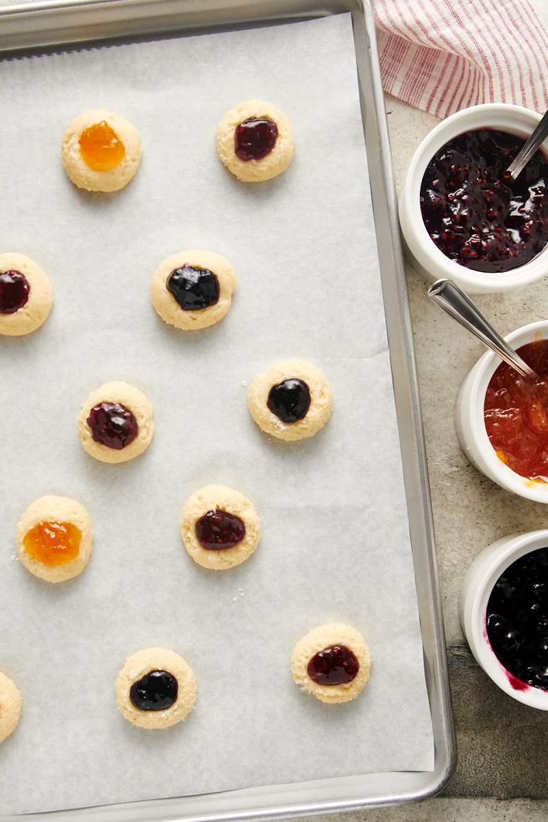 Cream Cheese Thumbprint Cookie dough filled with various jams on a parchment-lined baking sheet