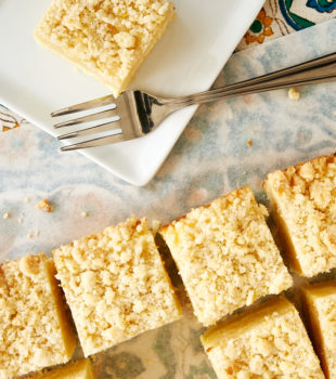 overhead view of slices of Lemon Cream Cheese Coffee Cake on a white plate and on white parchment paper