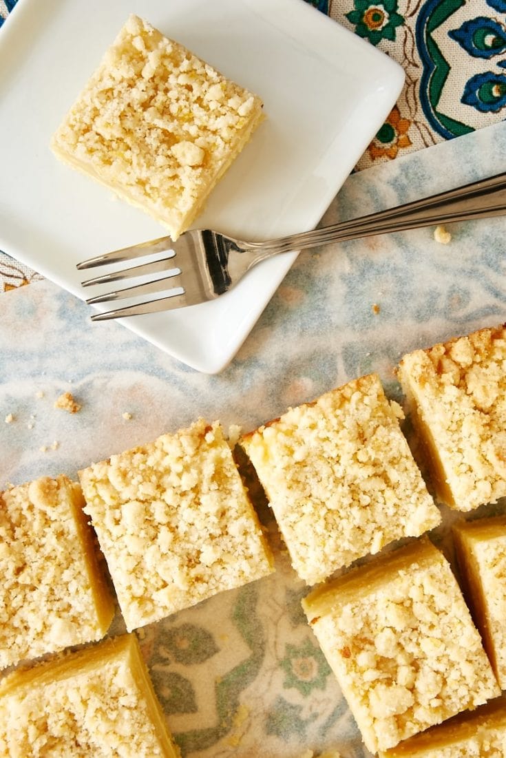 overhead view of slices of Lemon Cream Cheese Coffee Cake on a white plate and on white parchment paper