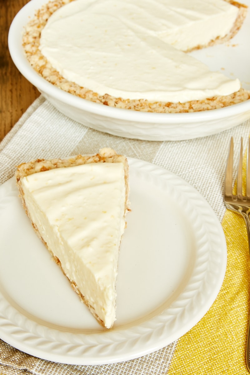 slice of Lemon Icebox Pie on a white plate with more pie in a white pie plate in the background