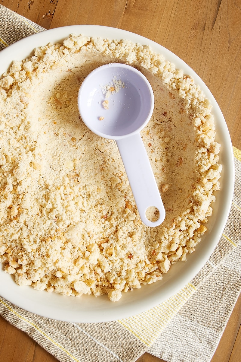 overhead view of toasted coconut crust being pressed into a white pie plate