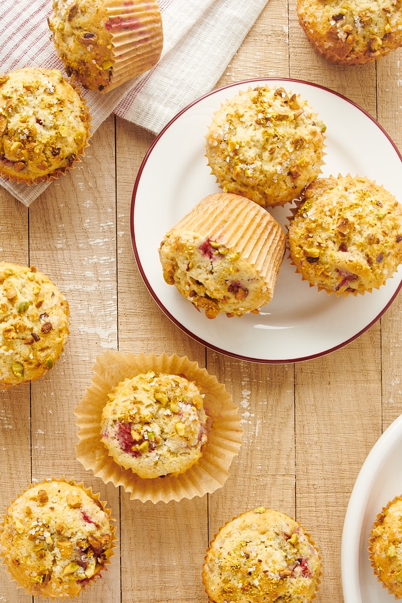 overhead view of Raspberry Pistachio Muffins on white plates and a light brown wooden surface