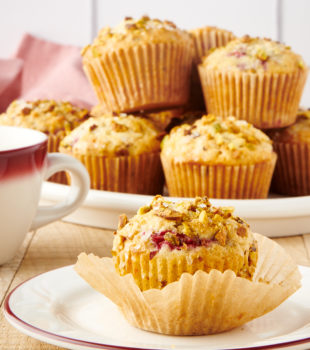 a partially unwrapped Raspberry Pistachio Muffin on a red-rimmed white plate with more muffins on a plate in the background
