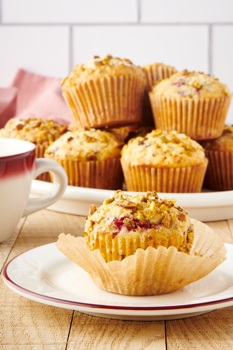 a partially unwrapped Raspberry Pistachio Muffin on a red-rimmed white plate with more muffins on a plate in the background