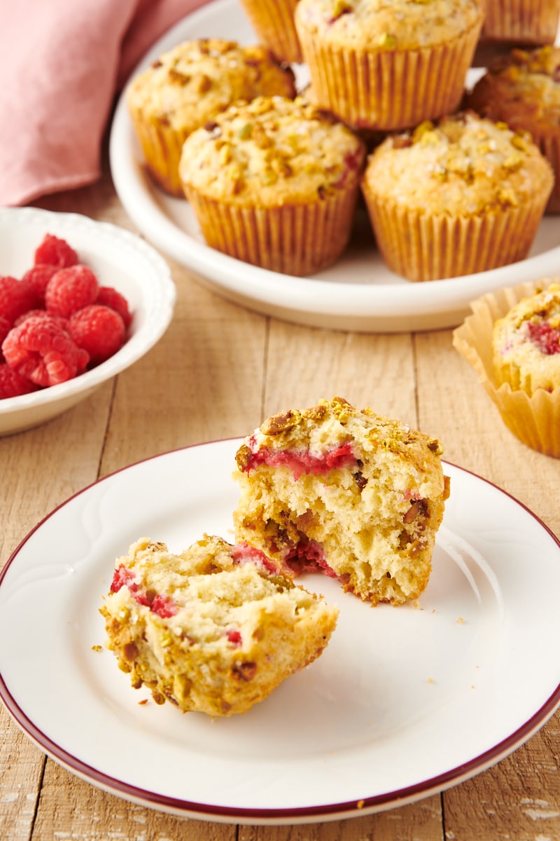 two halves of a Raspberry Pistachio Muffin on a white plate with more muffins in the background