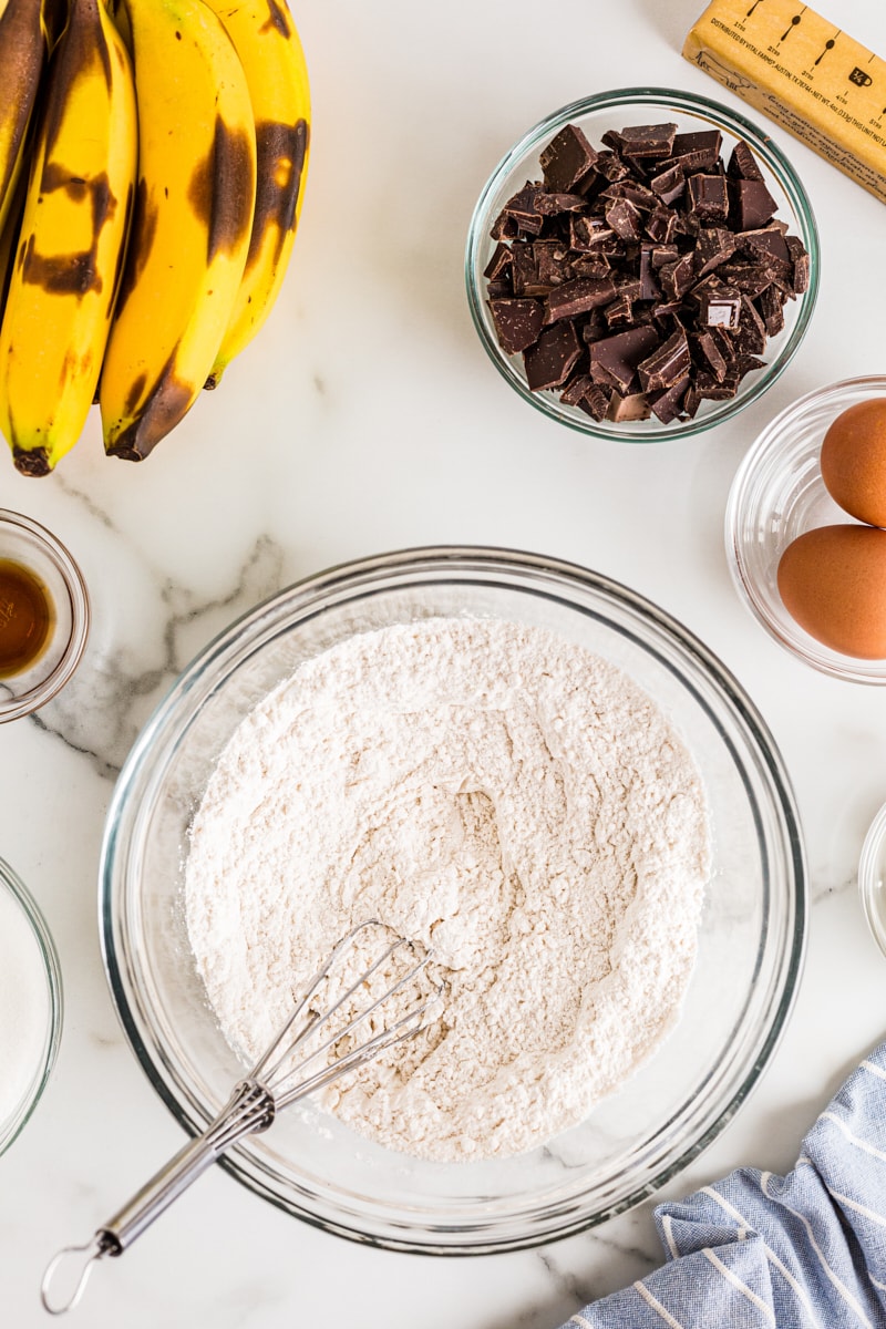 Dry ingredients for banana bread in glass bowl with whisk