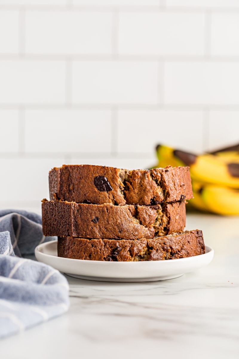 Three slices of Chocolate Chunk Banana Bread on plate next to tea towel