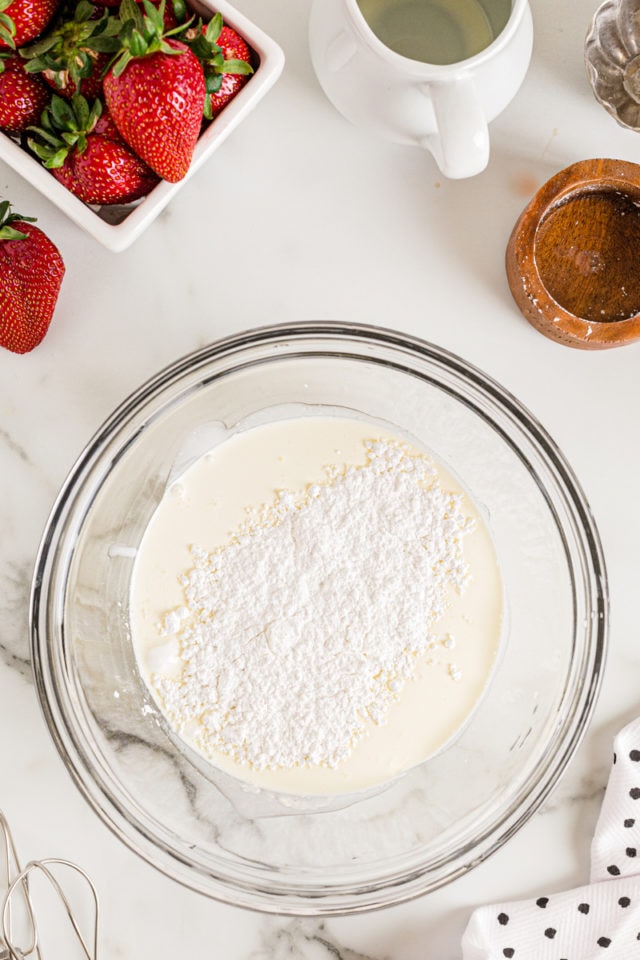 Overhead view of powdered sugar and cream in glass mixing bowl