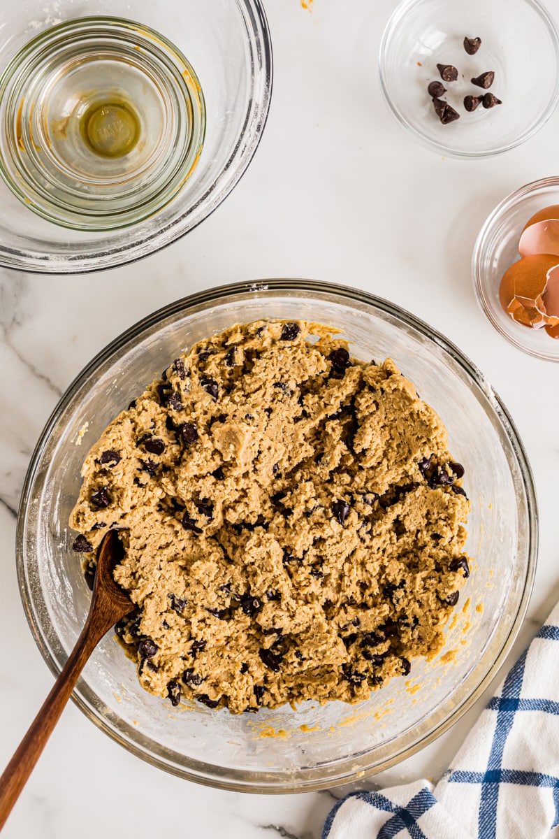 Overhead view of cookie dough in glass mixing bowl with wooden spoon