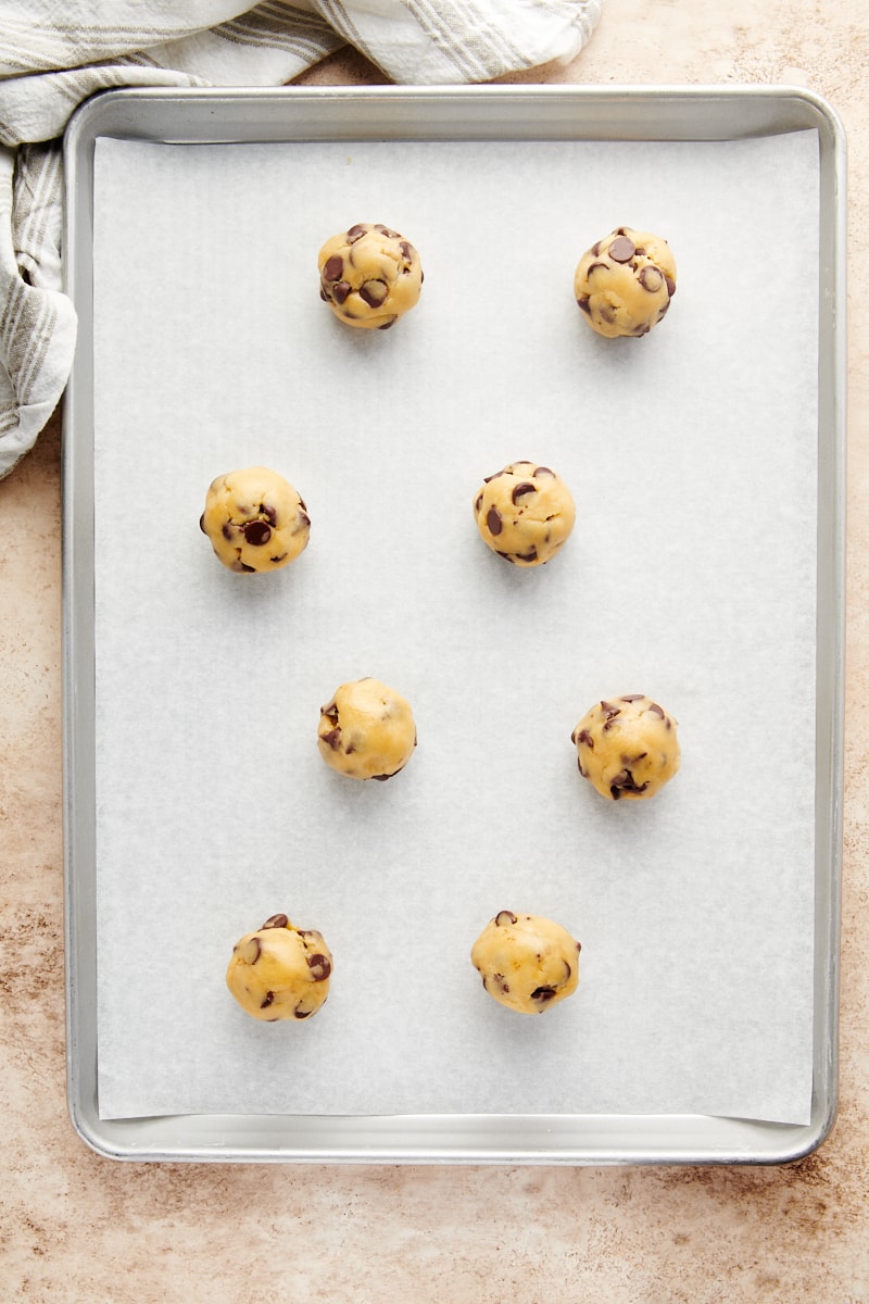overhead view of portioned and shaped Cheesecake-Stuffed Chocolate Chip Cookie dough on a parchment-lined baking sheet