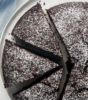 Overhead view of whole cocoa cake on plate, with three slices cut