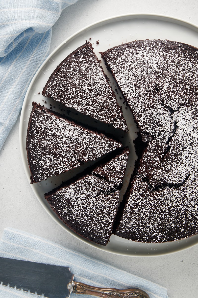 Overhead view of whole cocoa cake on plate, with three slices cut