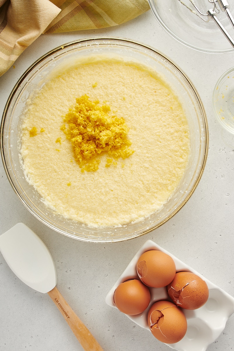 overhead view of lemon zest added to lemon curd mixture in a glass mixing bowl