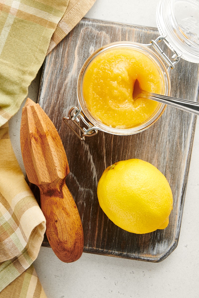 overhead view of an opened jar of lemon curd on a wooden cutting board