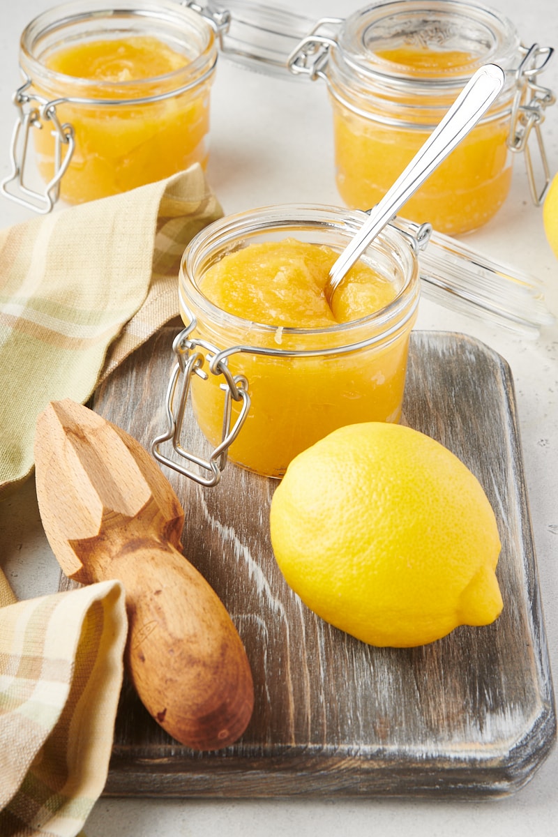 a glass jar of lemon curd on a wooden cutting board with a lemon and citrus juicer