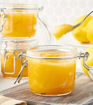 lemon curd in a glass jar with a spoonful above