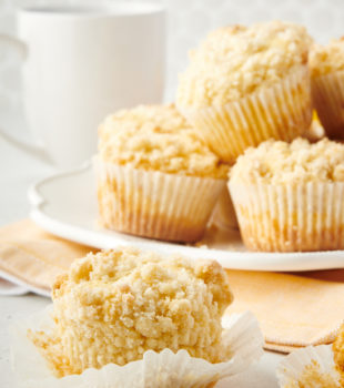an unwrapped lemon crumb muffin with a plate of muffins in the background