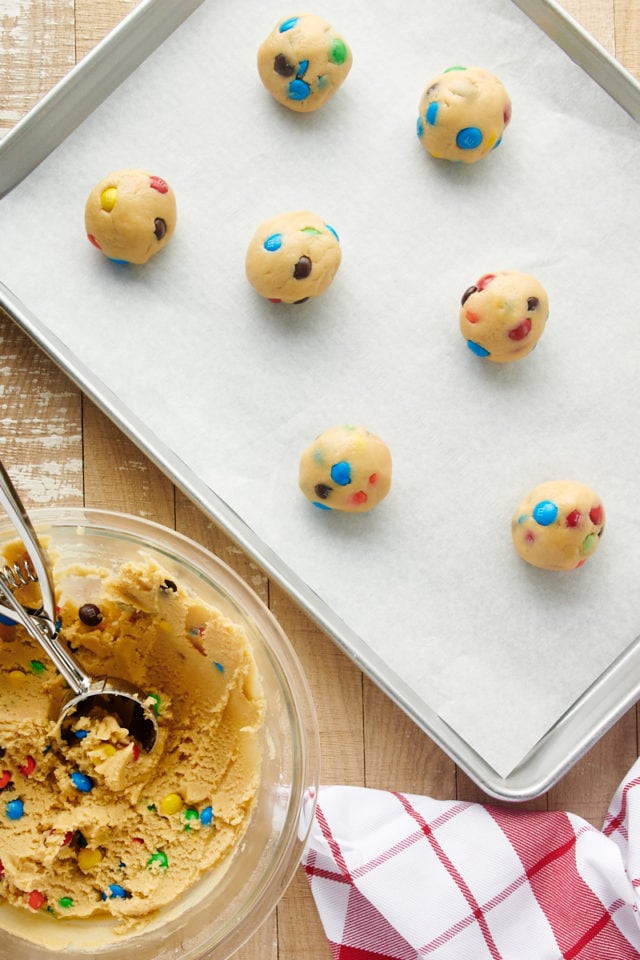 Overhead view of M&M cookie dough balls on parchment-lined sheet