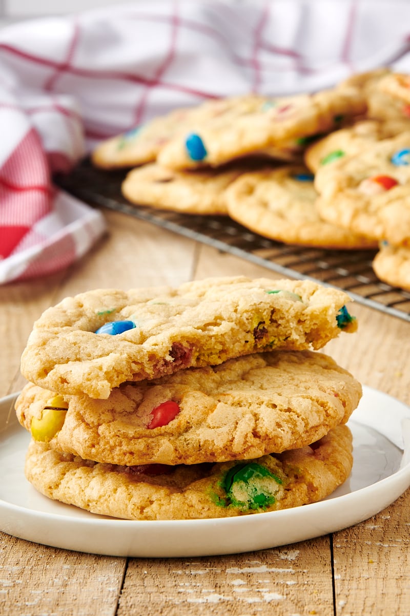 3 M&M cookies stacked on plate with one bitten