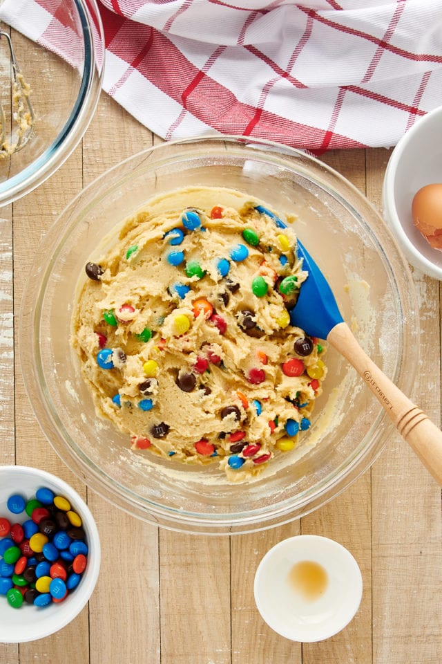 M&M cookie dough in glass mixing bowl with spatula
