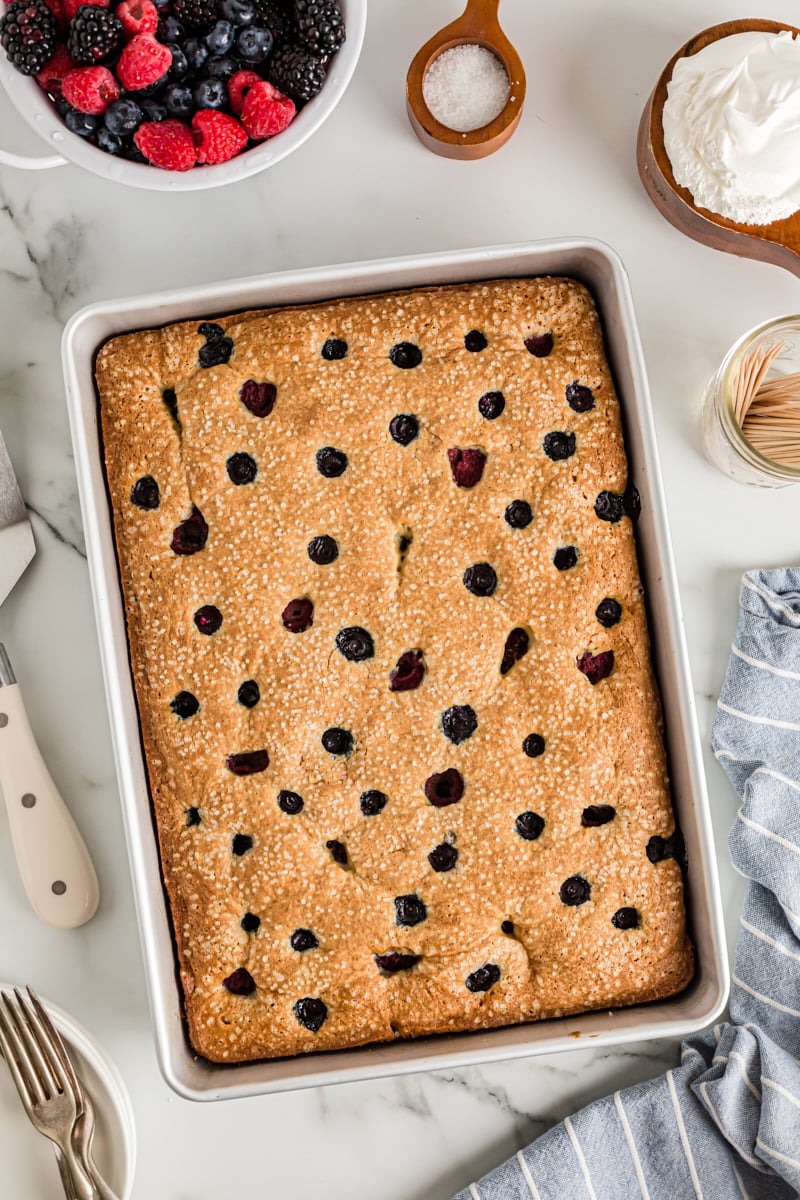 Overhead view of berry vanilla cake in pan with bowl of berries and whipped cream