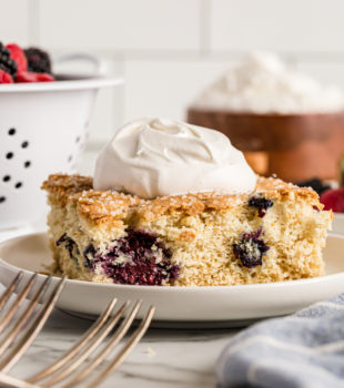 Square of berry vanilla cake on plate with dollop of whipped cream