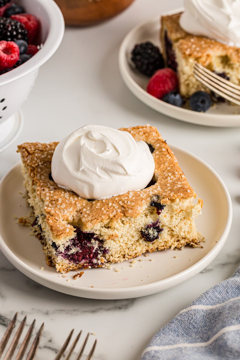 Square of berry vanilla cake on plate with dollop of whipped cream