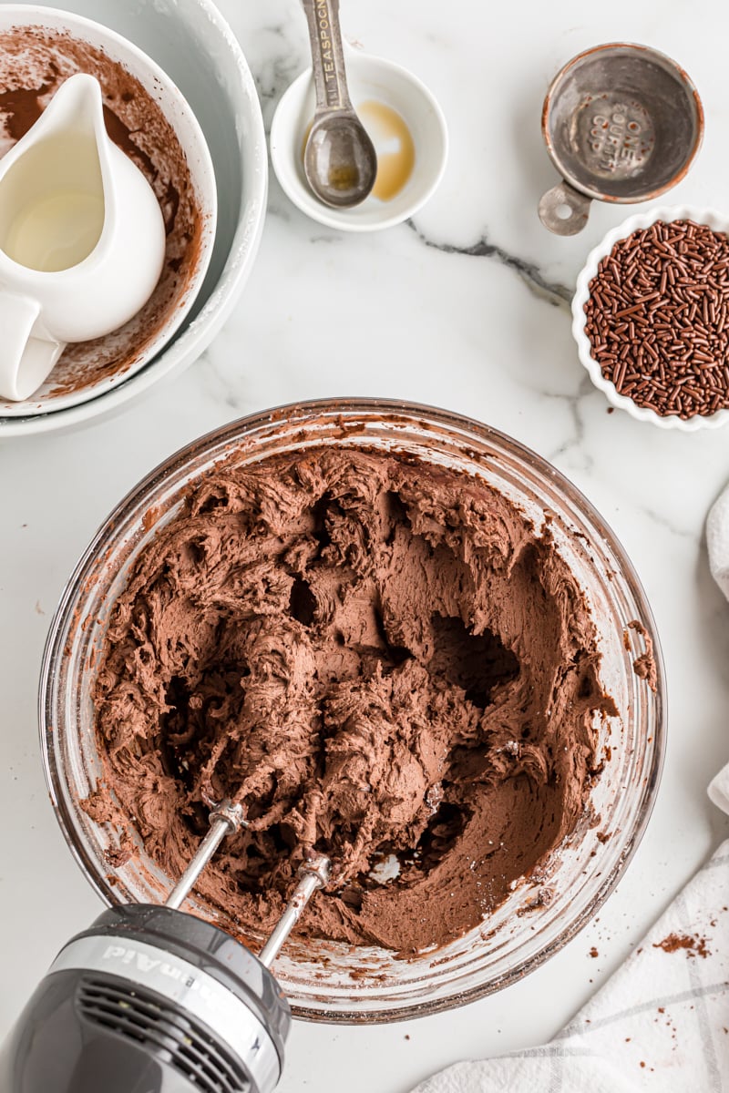 overhead view of partially mixed chocolate buttercream in a glass mixing bowl