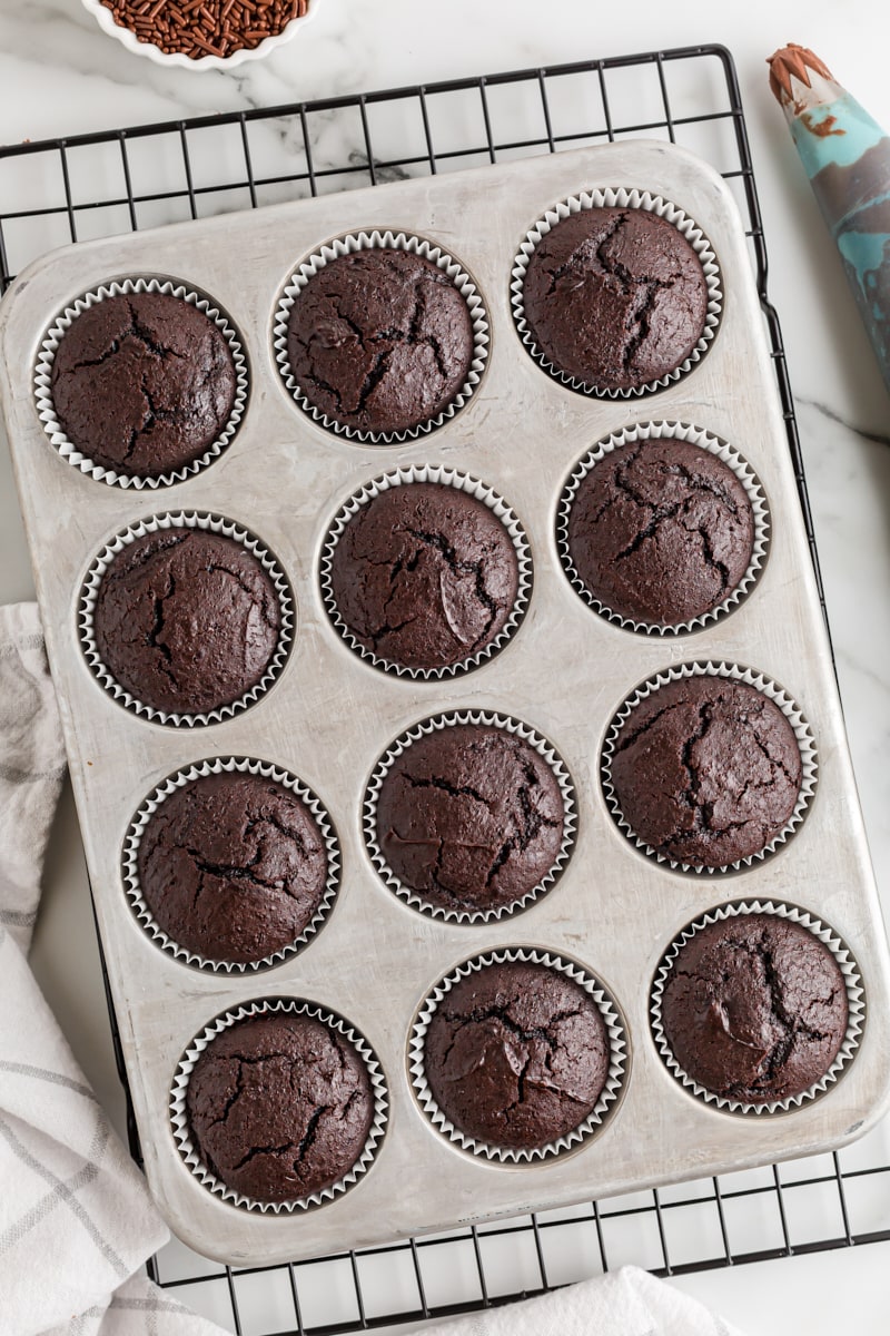 overhead view of freshly baked chocolate cupcakes in a muffin pan on a wire cooling rack