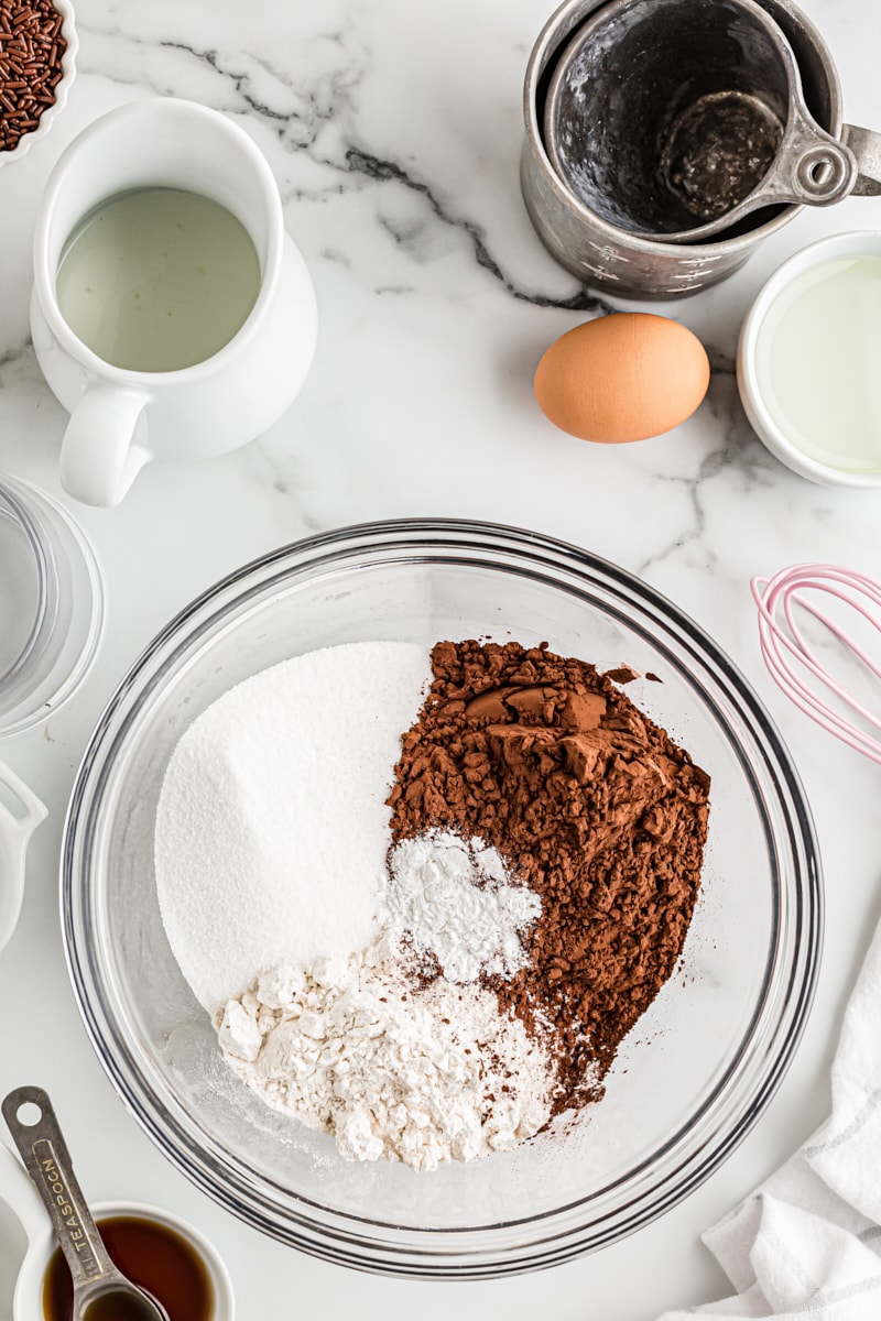 overhead view of flour, sugar, cocoa powder, and baking powder in a glass mixing bowl