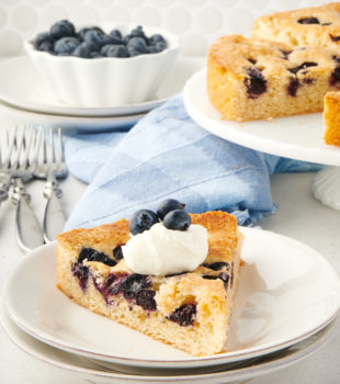 Slice of blueberry cake on plate with whipped cream and blueberries