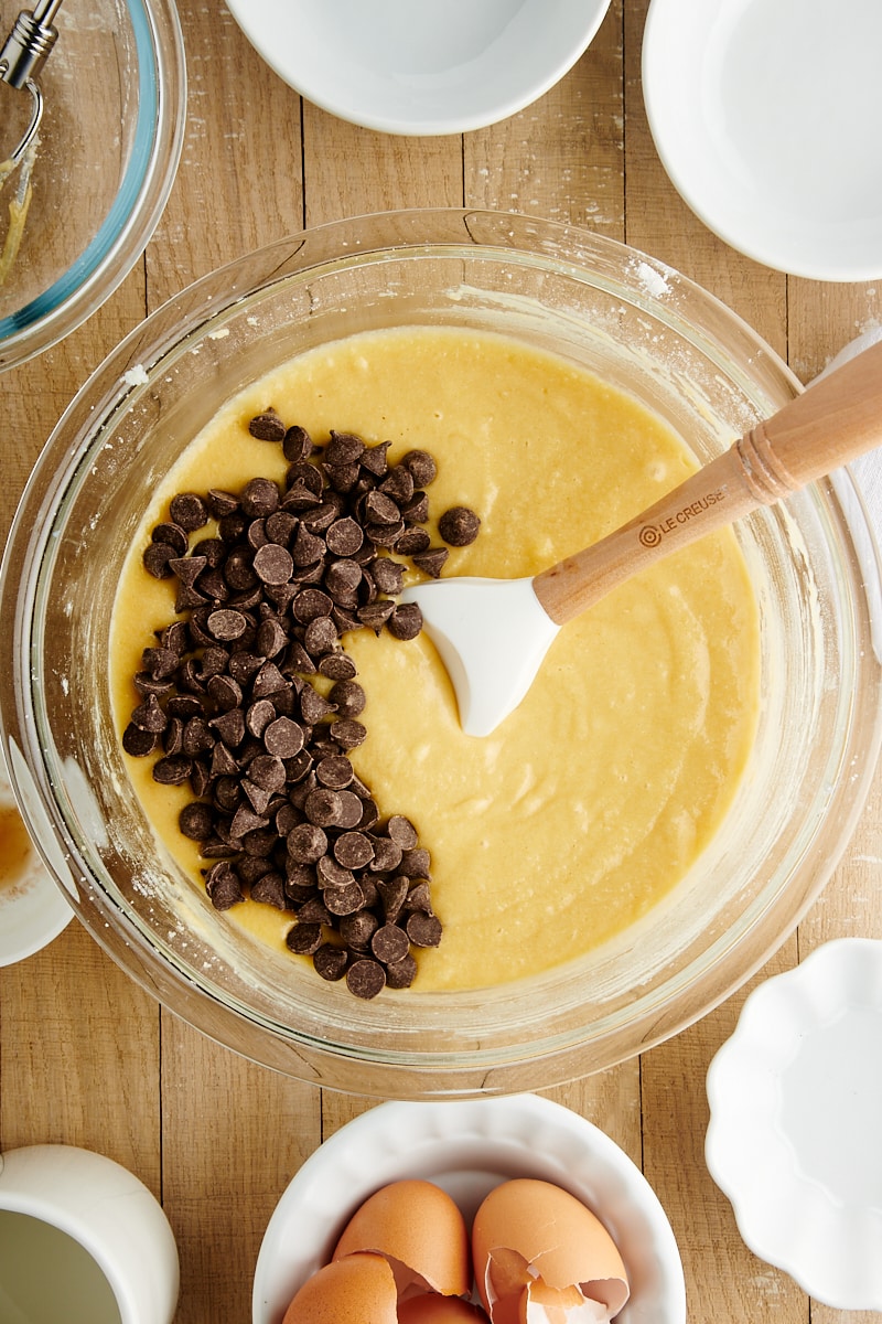 overhead view of chocolate chips added to cake batter in a glass mixing bowl