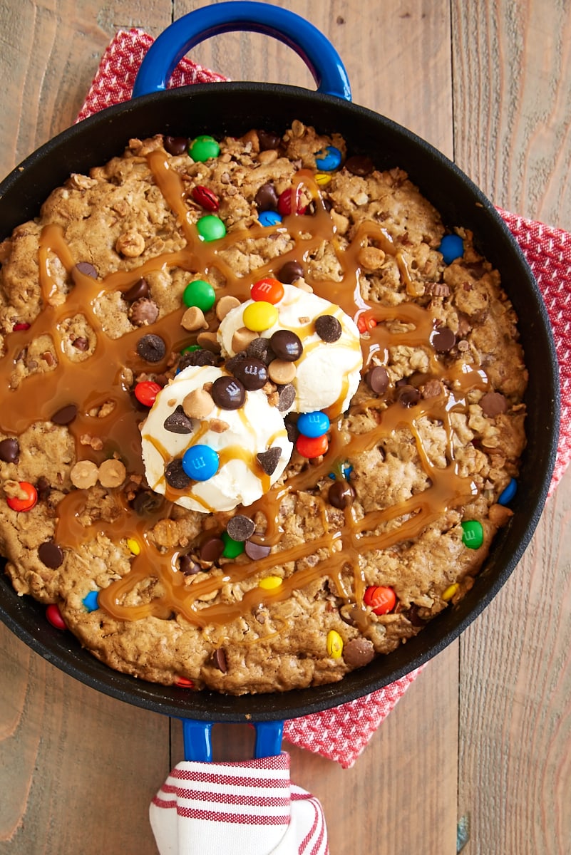 Overhead view of monster skillet cookie in cast iron skillet with ice cream, caramel, and M&Ms on top