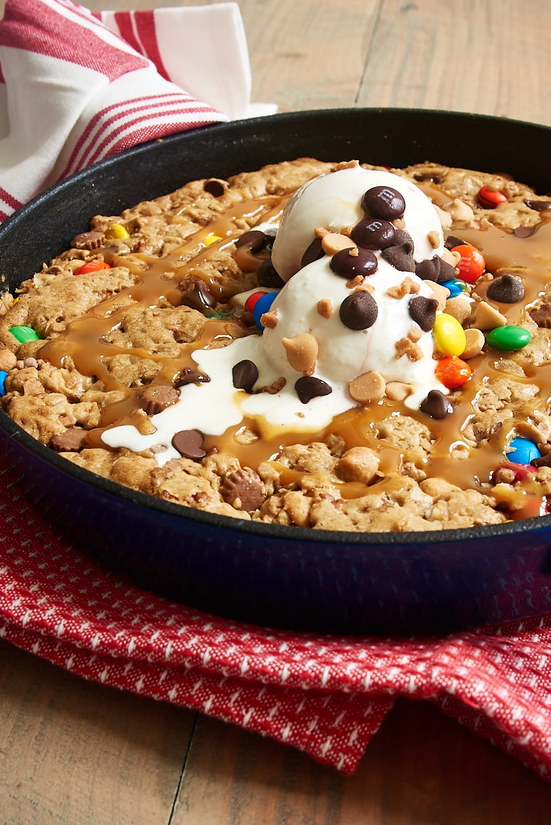 Cast iron skillet cookie topped with ice cream, chocolate chips M&Ms, and caramel