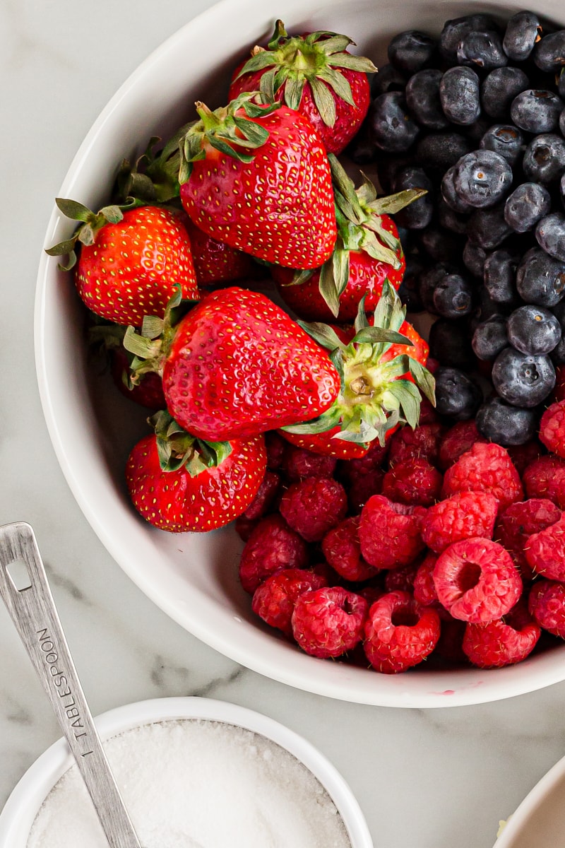 overhead view of strawberries, blueberries, and raspberries in a white bowl