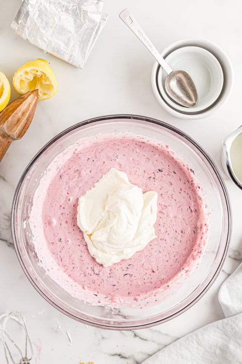 Overhead view of whipped cream added to bowl of cheesecake filling