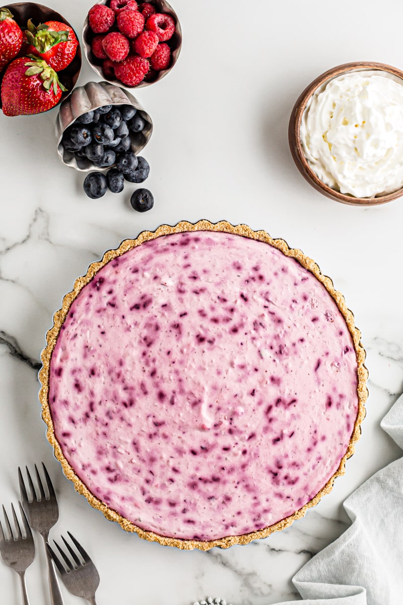 Overhead view of whole triple berry no-bake cheesecake in pan with garnishes in background