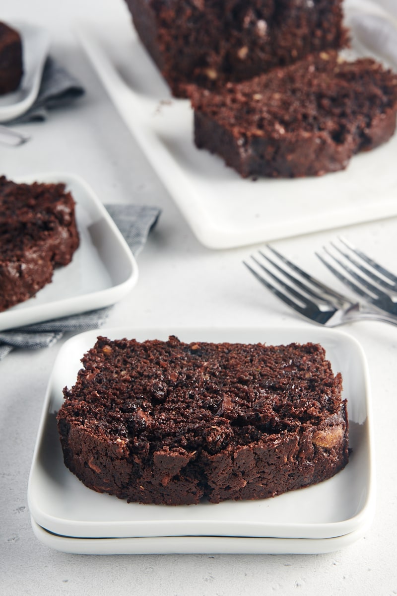 slice of Chocolate Zucchini Bread on a white plate with more servings in the background