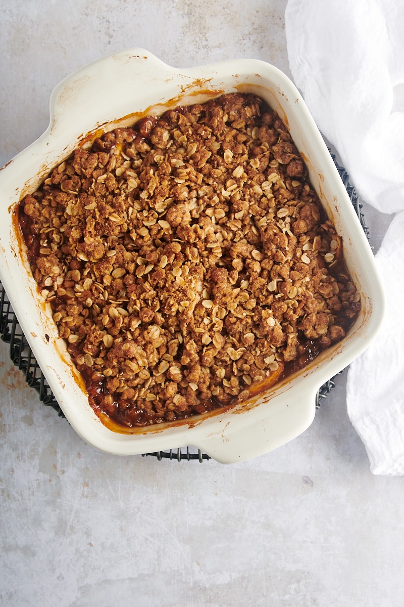 overhead view of freshly baked peach crisp in a white baking pan on a wire rack
