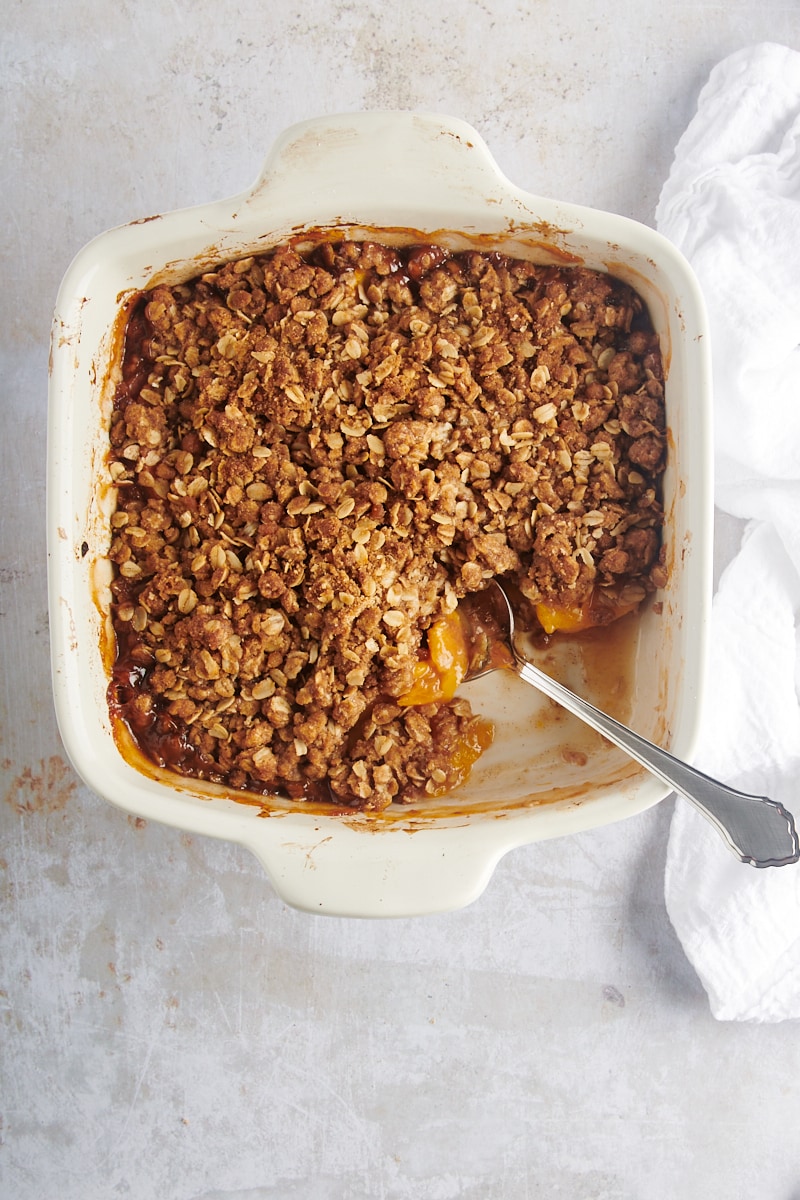 overhead view of peach crisp in a white baking dish with a serving spoon in one corner