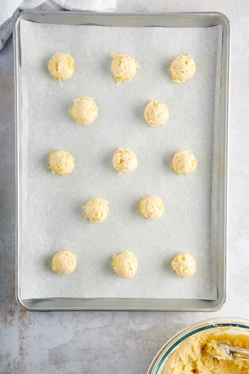 overhead view of scooped Pineapple Cream Cheese Cookie dough on a lined baking sheet