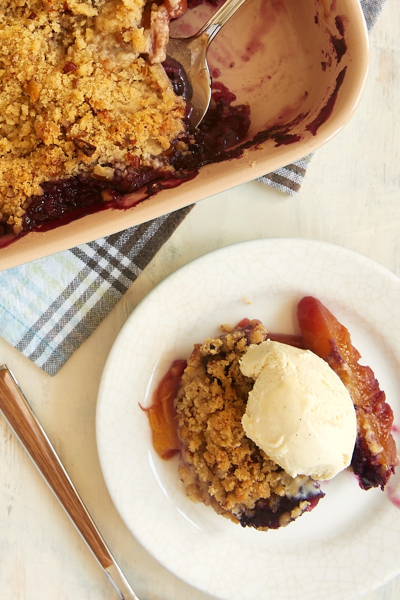 Overhead view of Blueberry Peach Crisp in baking dish and on dessert plate with vanilla ice cream