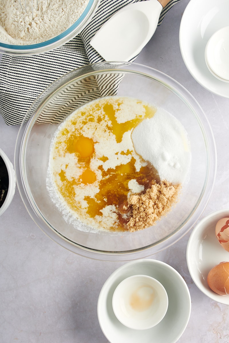 overhead view of melted butter, brown sugar, sugar, vanilla, and eggs in a glass mixing bowl